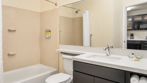 A modern bathroom with a bathtub, toilet, and shower. It includes a vanity with a sink and a large mirror. - Candlewood Suites Destin-Sandestin by IHG (Miramar Beach)