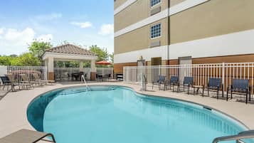 A swimming pool with lounge chairs and a covered seating area.