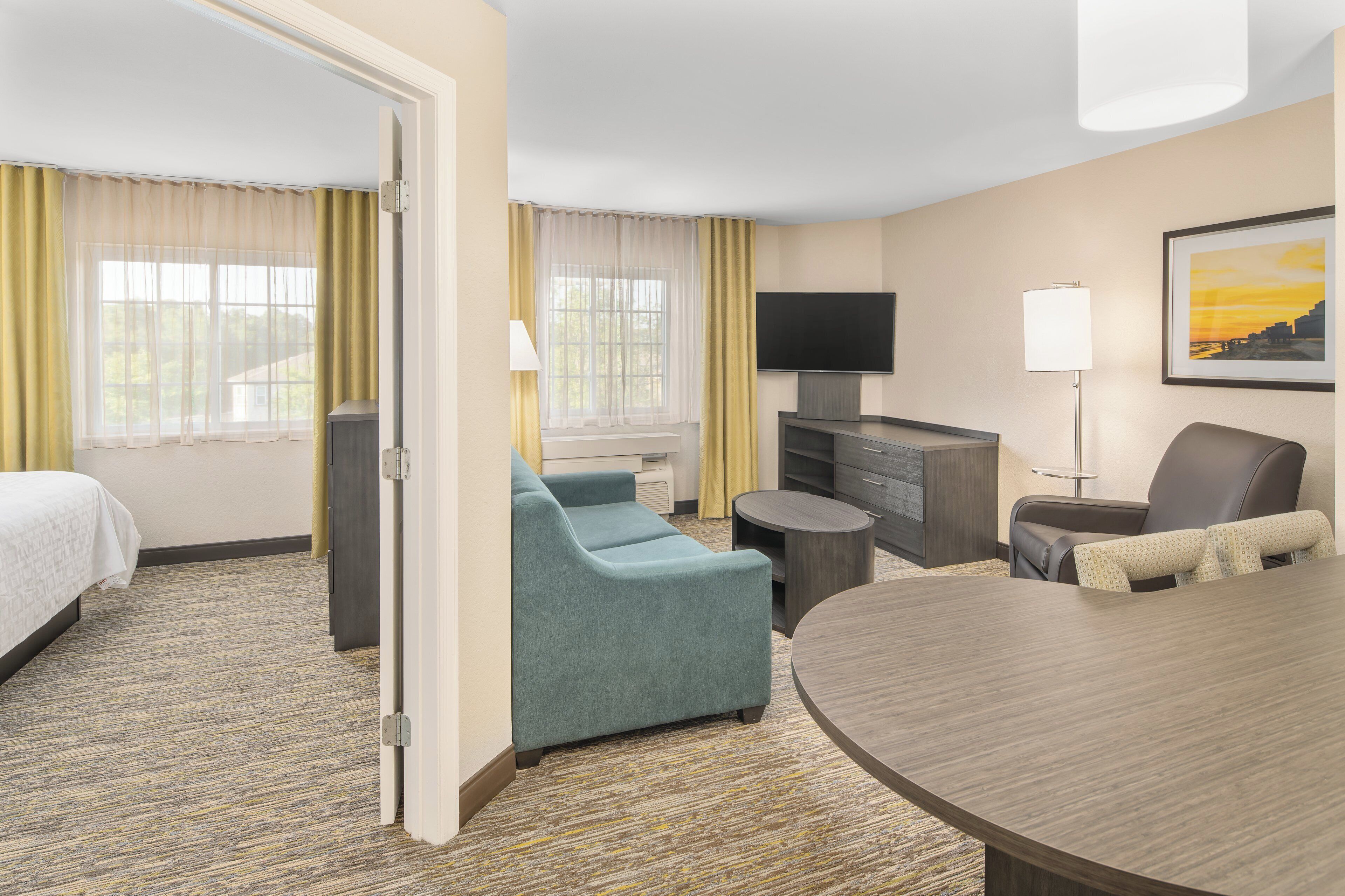 A hotel room with a bed, a sofa, a TV, a desk, and a dining table.