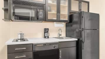 A compact kitchen with a microwave, coffee maker, sink, and a black refrigerator.