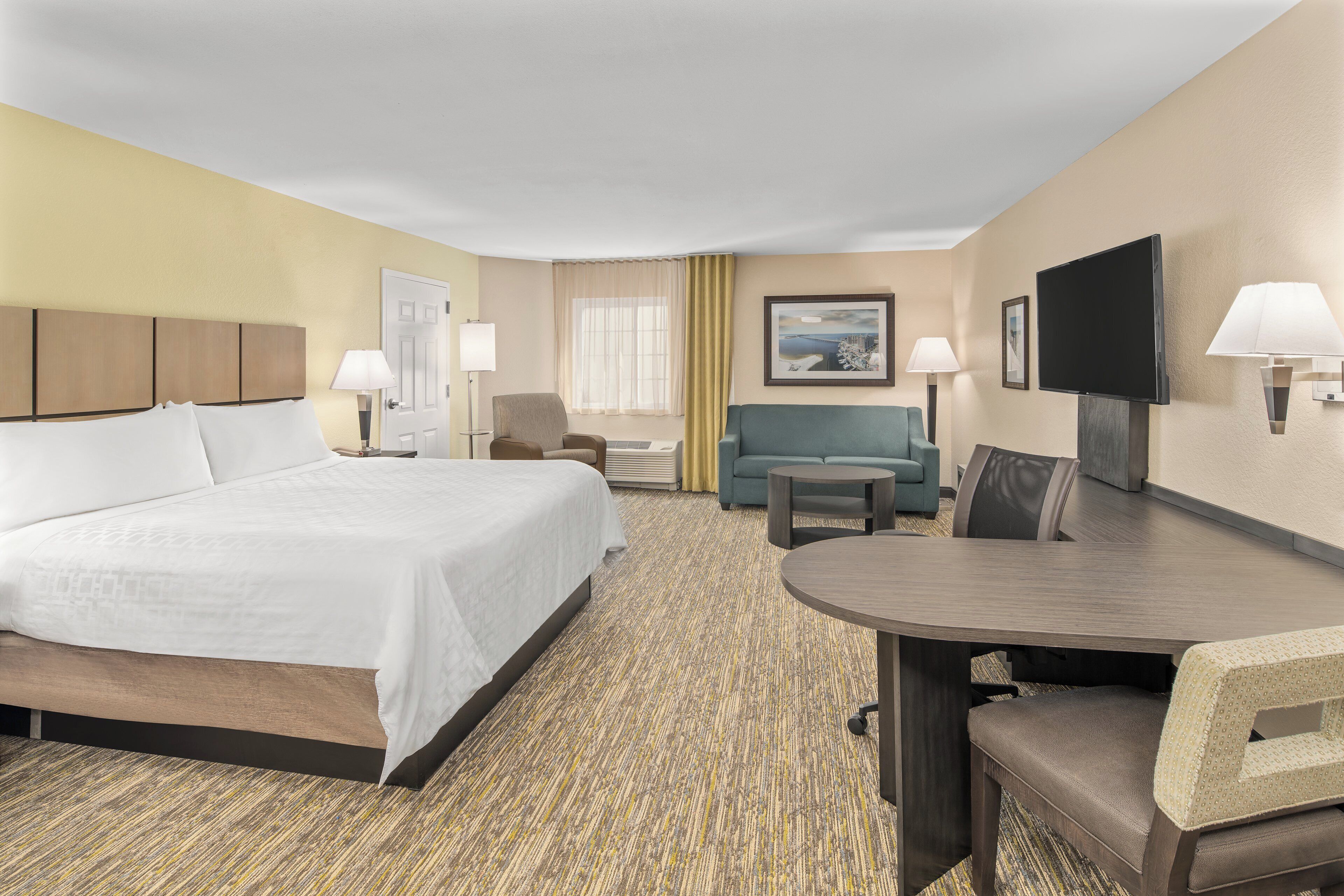 A hotel room with a bed, a sofa, a dining table, and a TV.