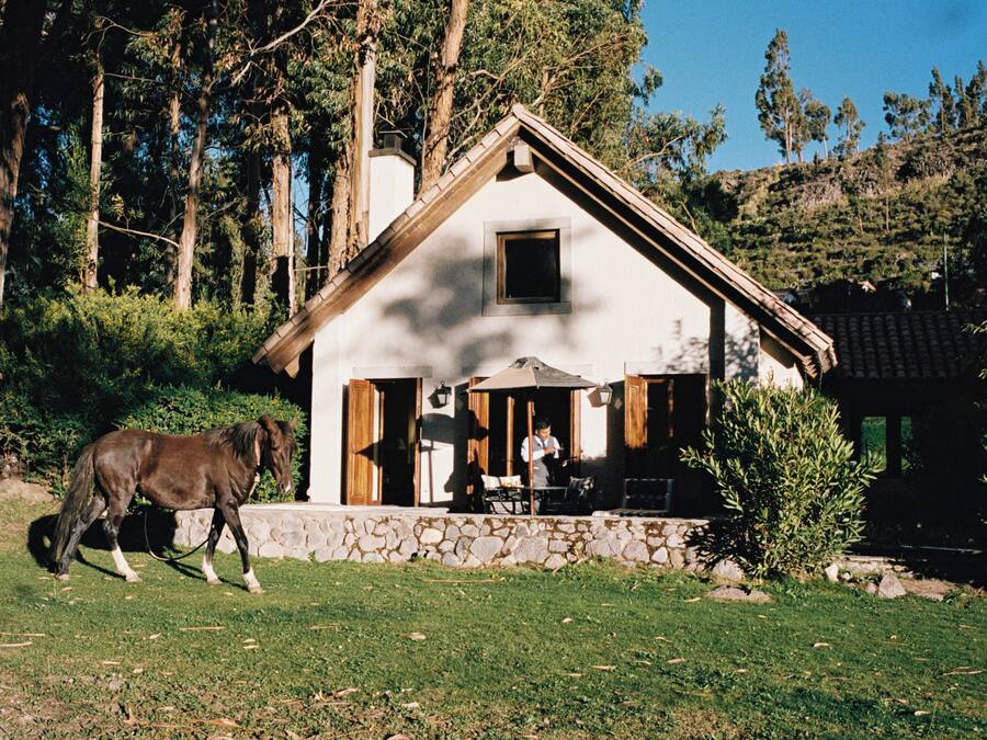 Una casa rústica con base de piedra, un porche de madera y un caballo pastando cerca.