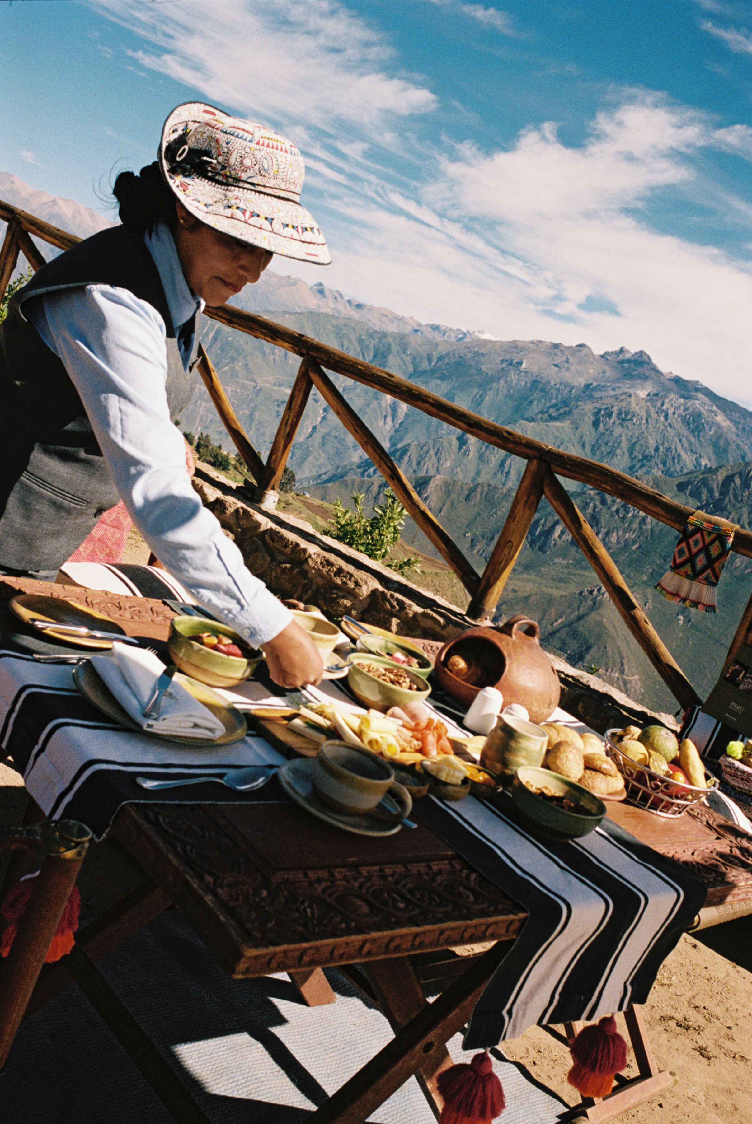 Una persona sirve comida en una mesa con montañas al fondo.
