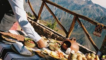 Una persona sirve comida en una mesa con montañas al fondo.