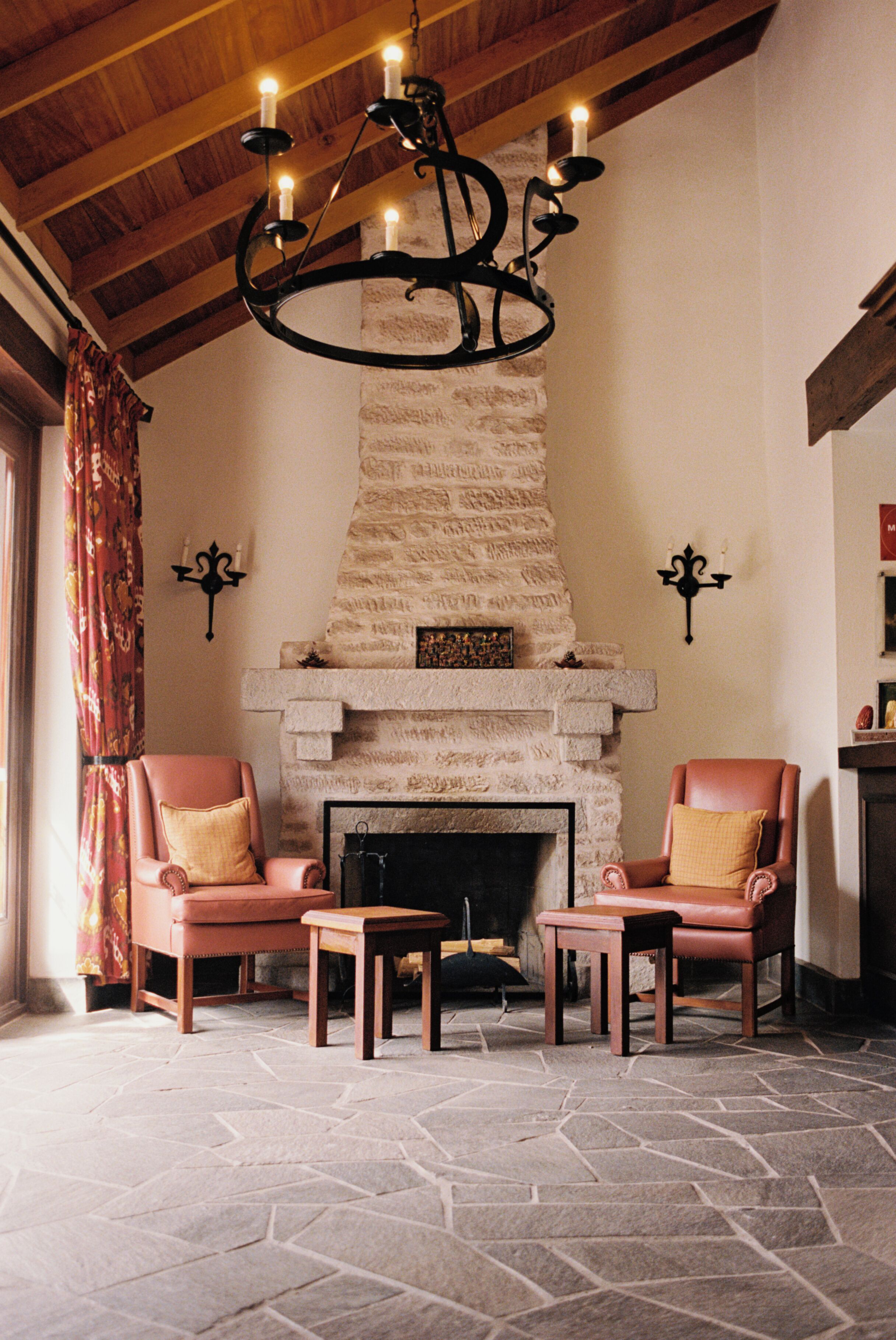 A room with a stone fireplace, two leather armchairs, a small table, and a chandelier.