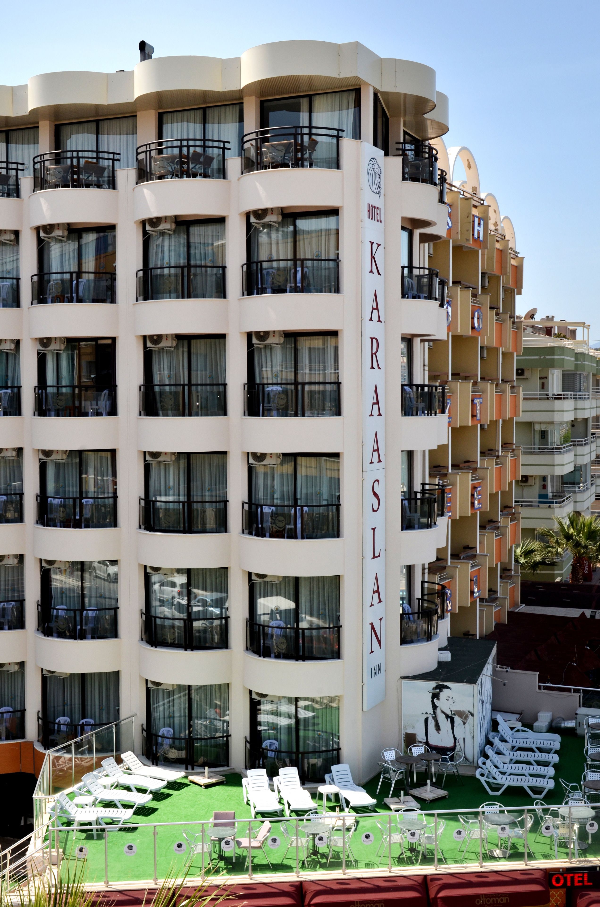 A multi-story hotel with balconies, a rooftop lounge area with sun loungers, and a clear view of the surrounding buildings.