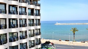 Ein mehrstöckiges Hotel mit Balkonen, die auf einen Strand und das Meer blicken.