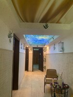 Un pasillo con techo de tragaluces, una zona de estar con una mesa y plantas decorativas.