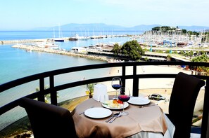 A table set with plates, cutlery, and wine glasses, overlooking a marina with boats and a beach. - By Karaaslan Inn (Kusadasi)