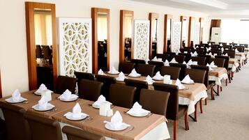 Een restaurantgedeelte van een hotel met meerdere gedekte tafels, elk met een witte tafelkleed, bruine stoelen en netjes opgemaakte servetten en bestek.
