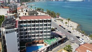 Ein mehrstöckiges Hotel mit Pool auf dem Dach, gelegen in Küstennähe mit Blick auf das Meer und einem Kreuzfahrtschiff in der Ferne.