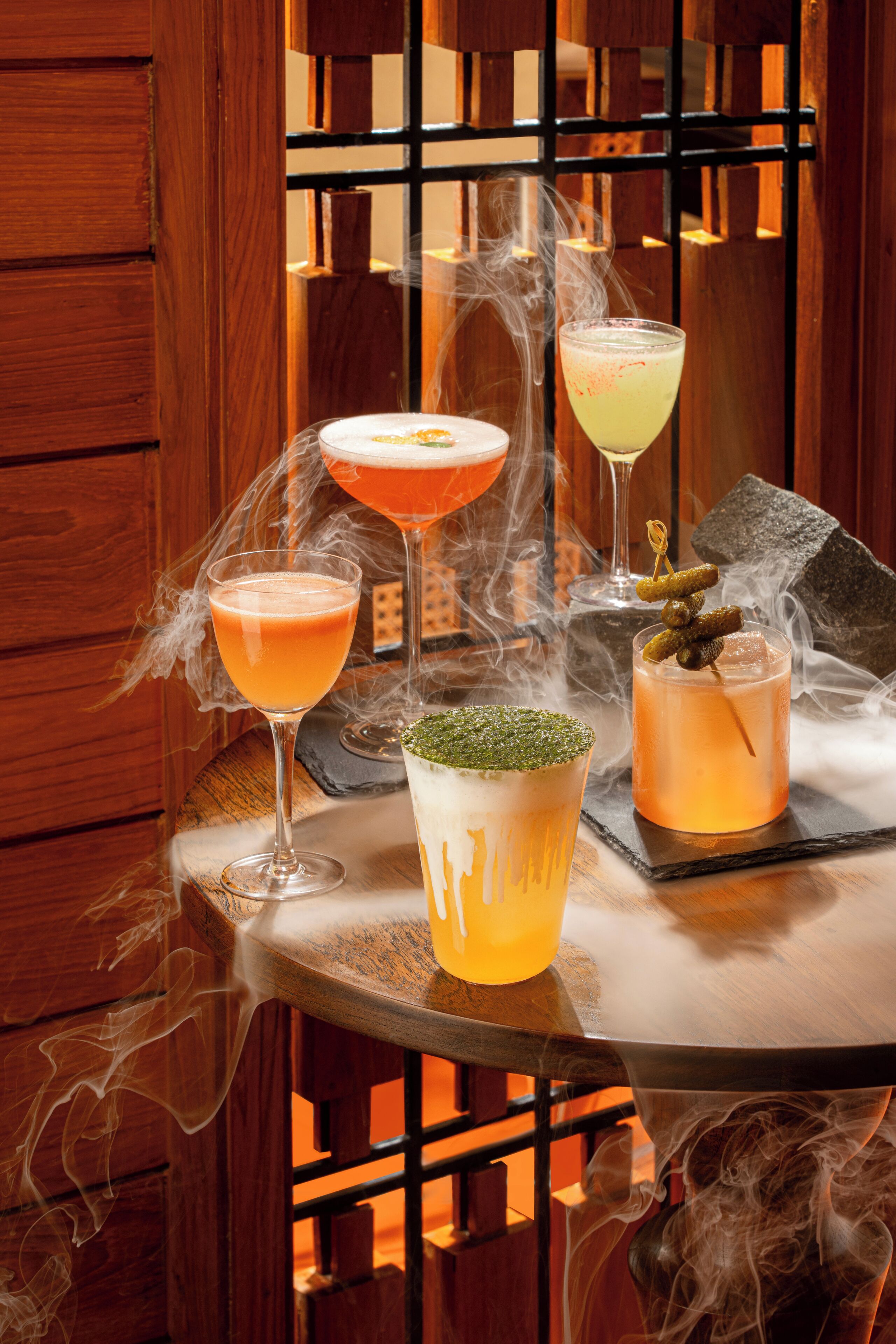 A table with four glasses of cocktails, smoke effects, and a decorative stone.