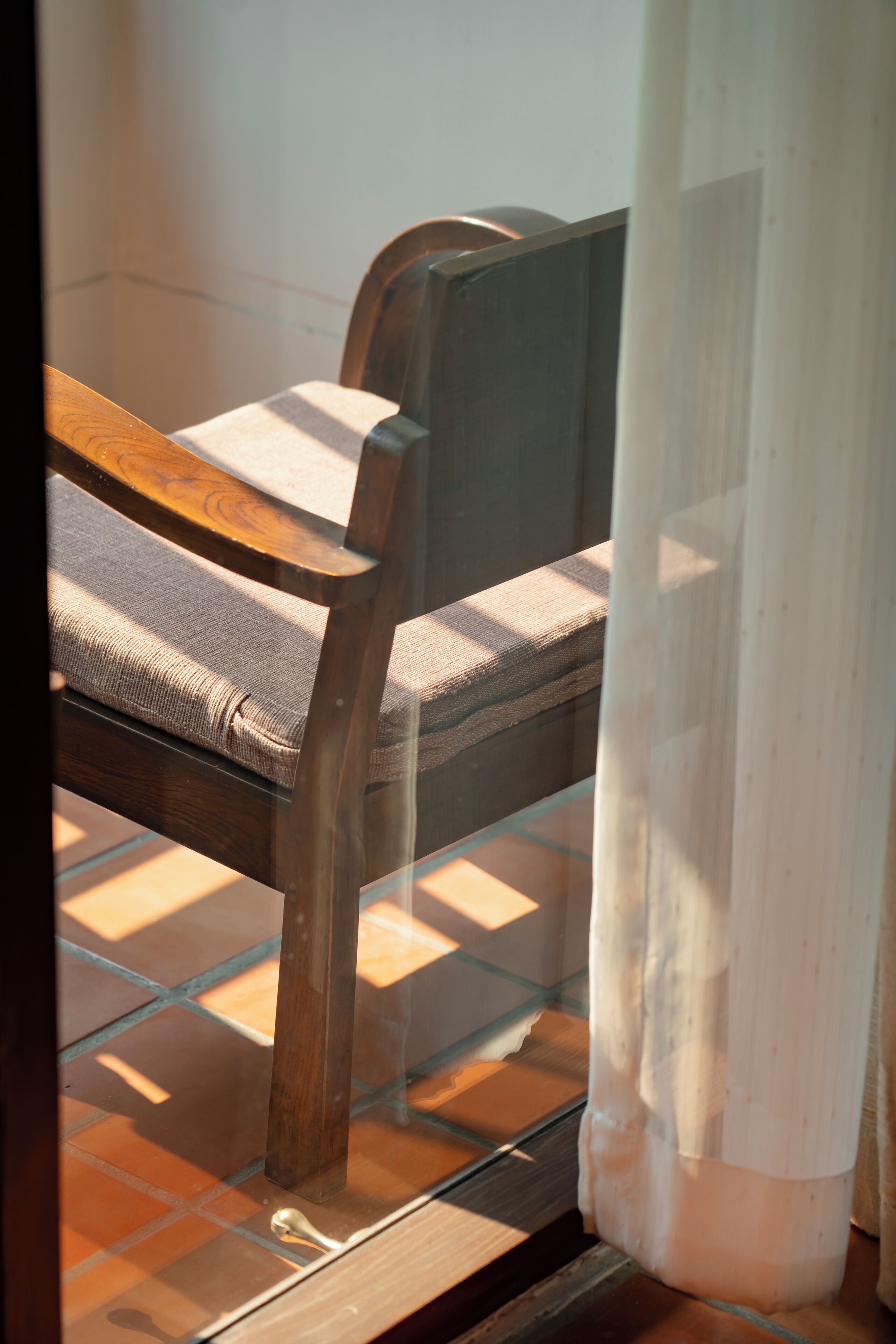 A wooden chair with a cushion, positioned near a window with a curtain partially drawn.