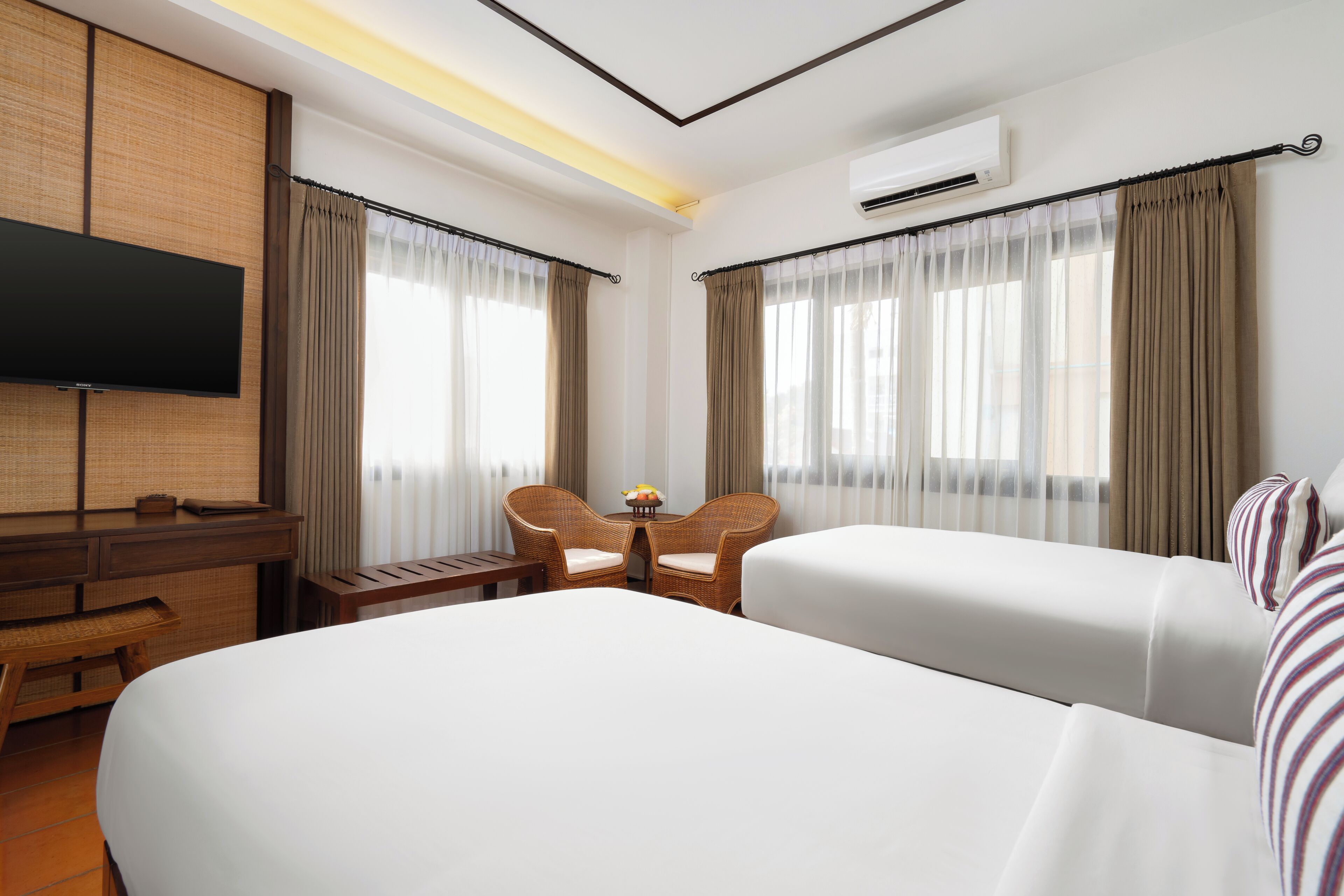 Une chambre d’hôtel avec un grand lit, deux chaises, une petite table, un téléviseur et un appareil de climatisation.