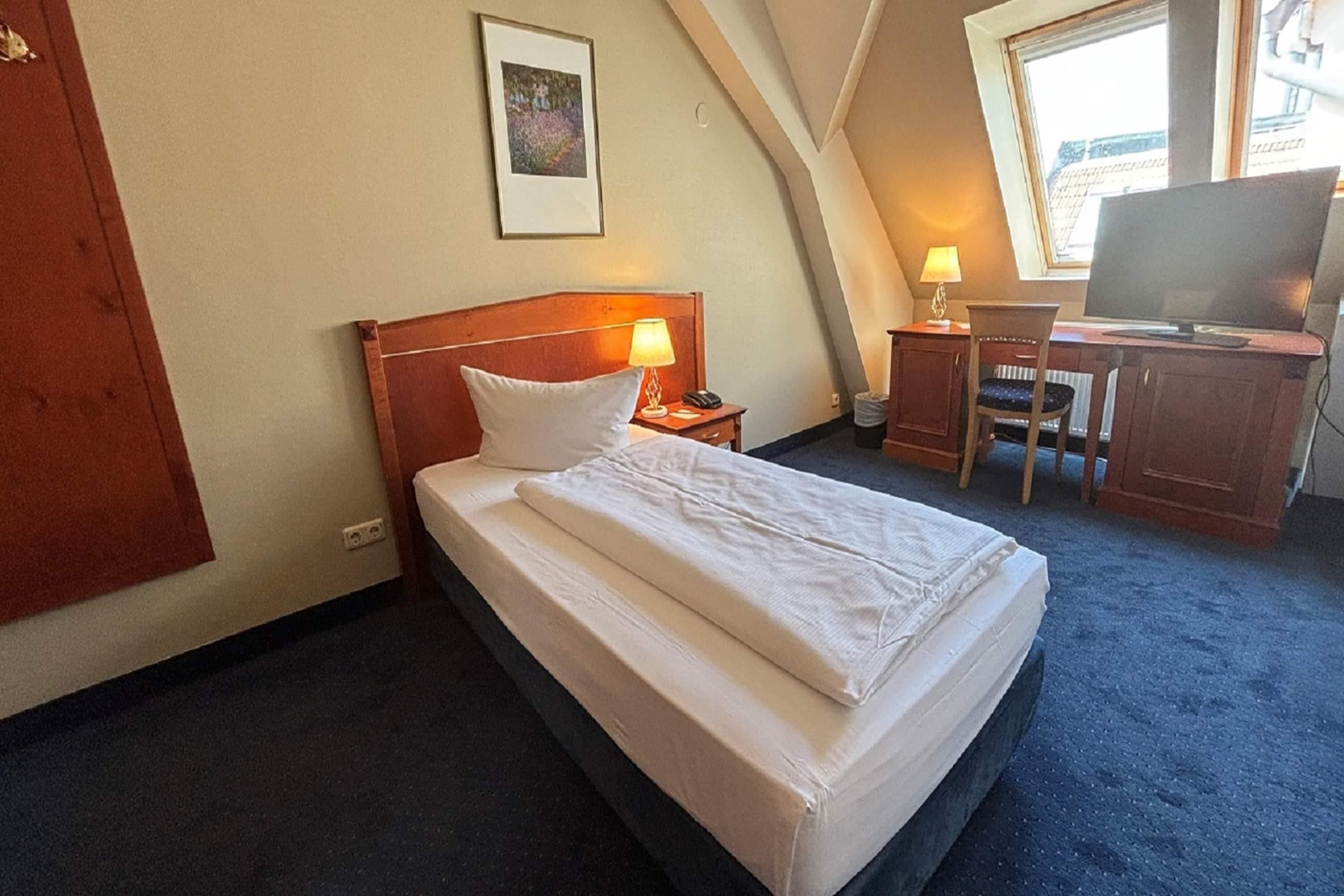 A hotel room with a bed, a desk with a chair, a television, and a window.