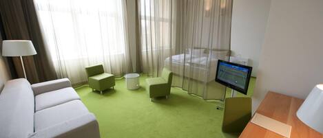 A hotel room with a green carpet, a bed, a TV, a desk, and a chair.