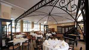 A dining area with tables set for service, a grand piano, and a high ceiling with decorative metalwork. - Wyndham Garden Berlin Mitte (Berlin)