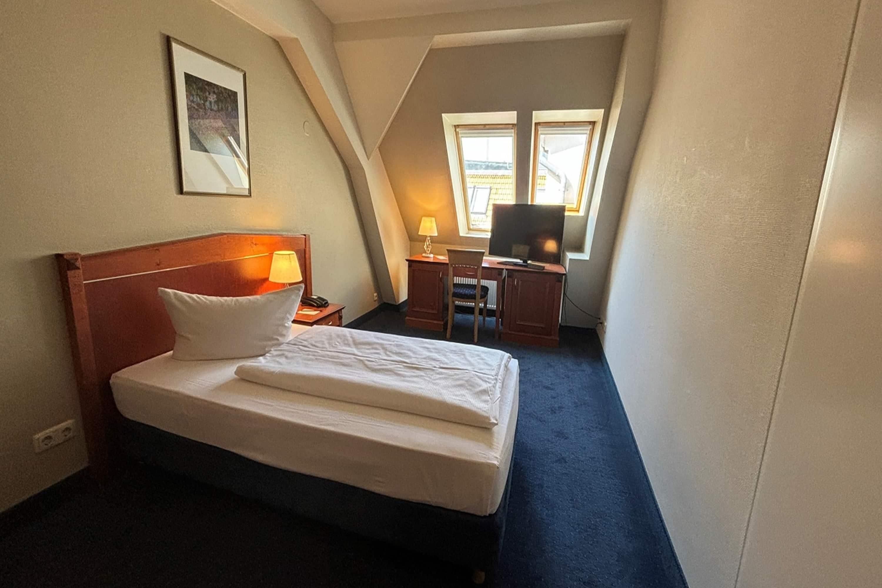 A hotel room with a bed, a desk with a computer, and a window.