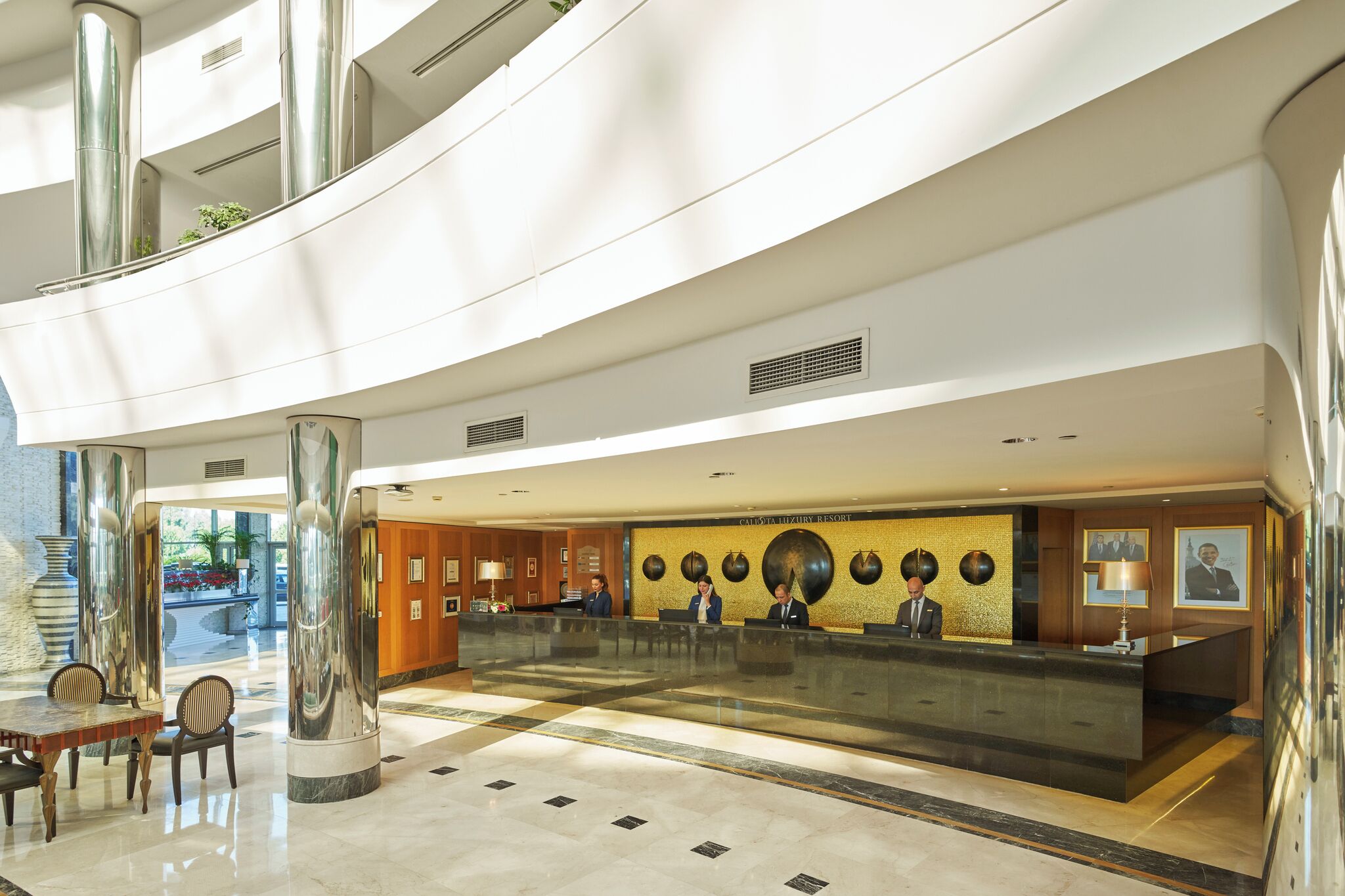 A modern hotel lobby with a reception desk, seating area, and large columns.