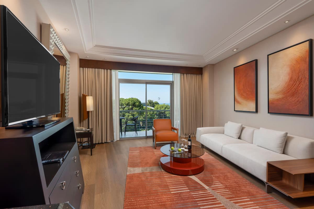 A modern hotel room with a large TV, a sofa, a coffee table, and a balcony with a view.