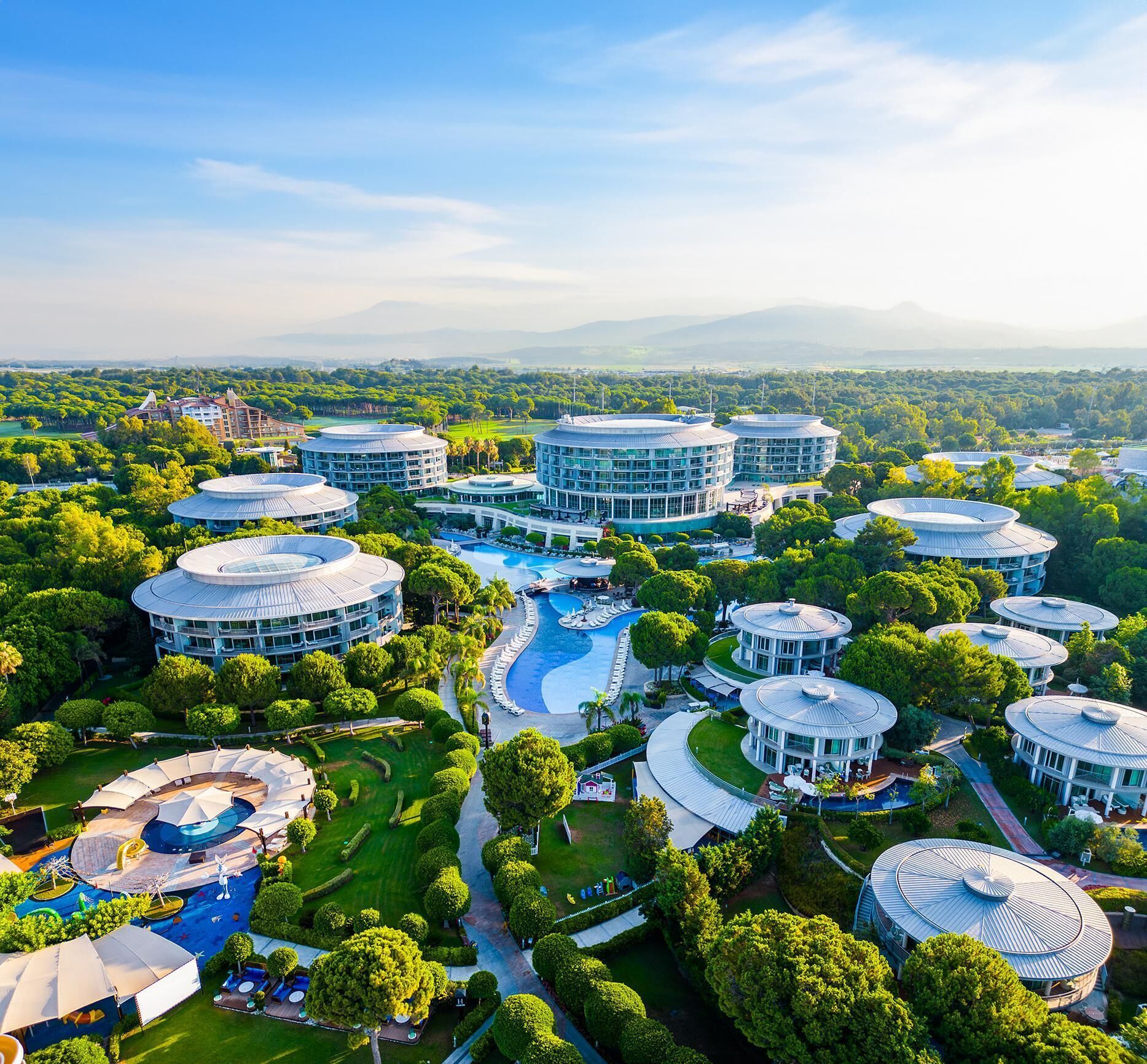 Ein Resort mit mehreren Gebäuden mit Runddächern, einem zentralen Schwimmbad und üppiger Bepflanzung.
