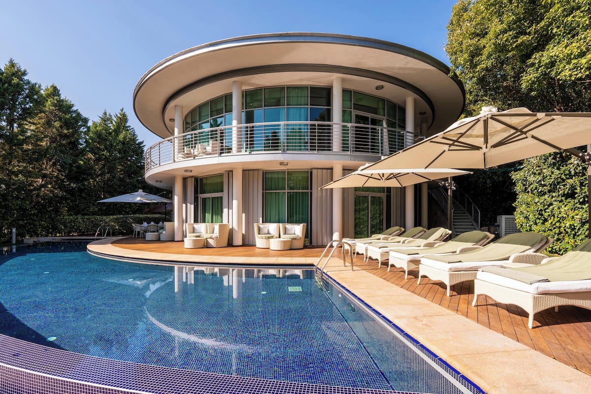 A modern house with a circular balcony, a swimming pool, and lounge chairs.