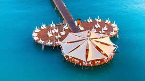 Vista aérea de una plataforma circular flotante con varias tumbonas y sombrillas, rodeada de agua turquesa.