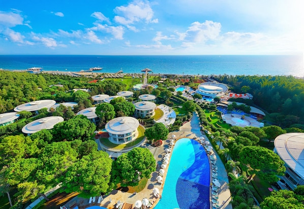 An aerial view of a resort with multiple round-roofed buildings, a large swimming pool, and a view of the ocean. - Calista Luxury Resort - All Inclusive (Serik)