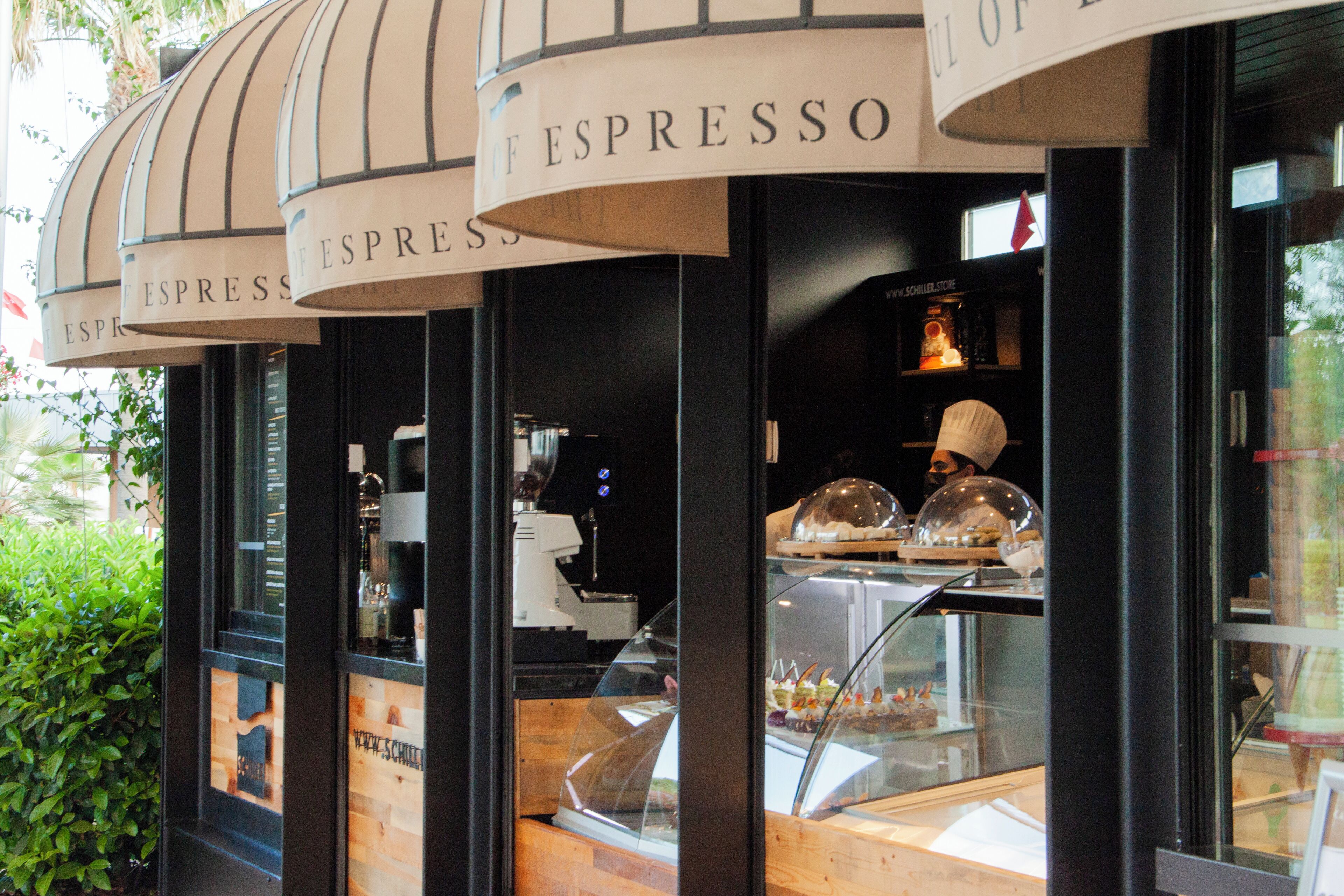 A coffee shop with multiple espresso signs and a display case with pastries.