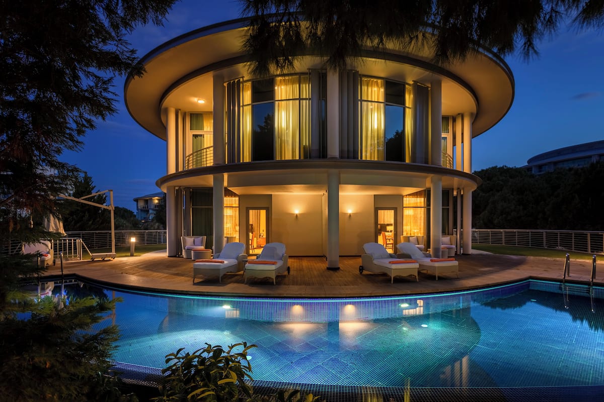 A modern, circular building with a pool and lounge chairs.