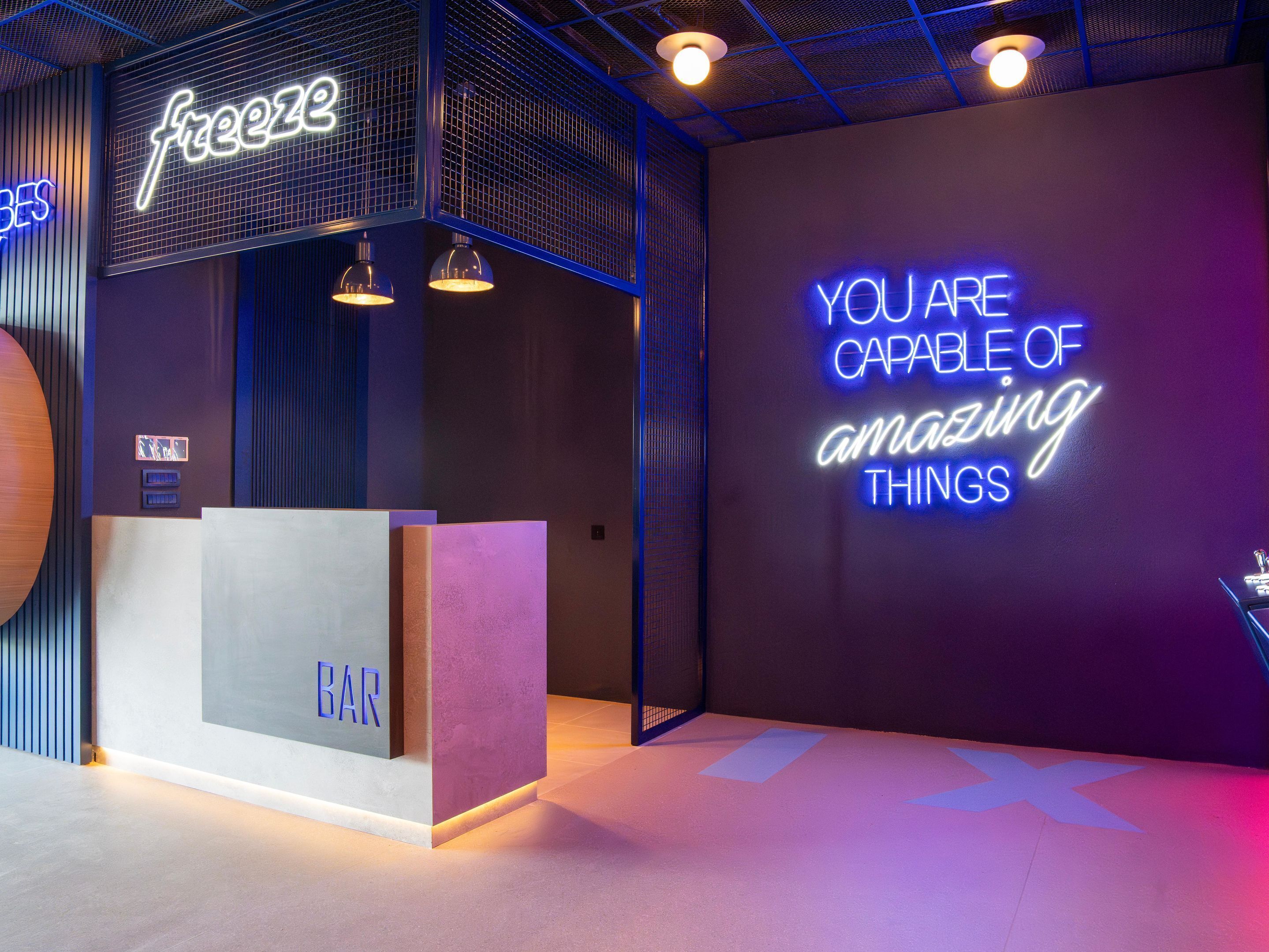 Un espace bar moderne agrémenté d’un panneau néon sur lequel on peut lire le mot « freeze » et d’un autre panneau indiquant : « VOUS ÊTES CAPABLE DE réaliser des choses extraordinaires ».