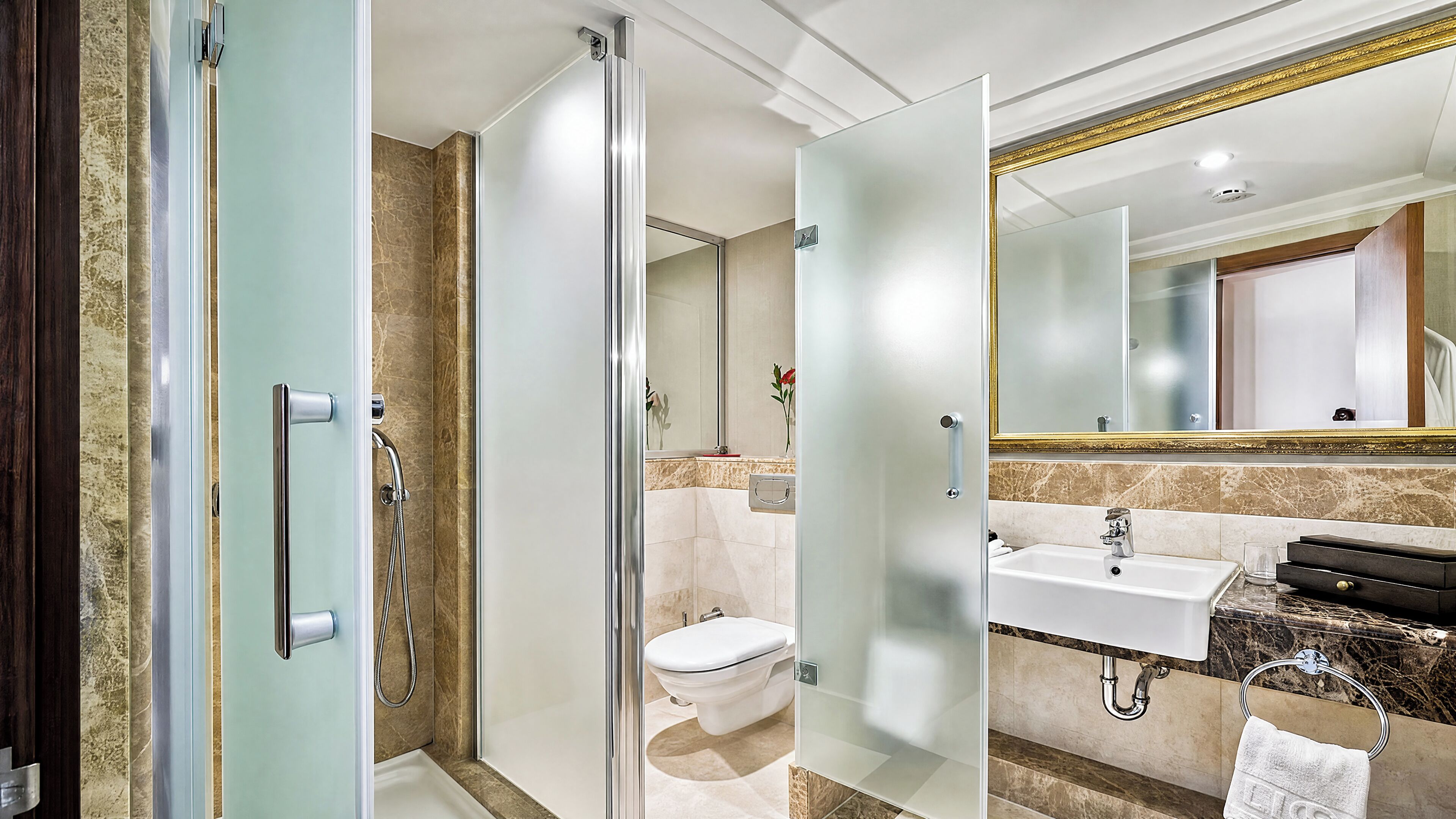 Une salle de bain moderne avec une douche à parois de verre, des toilettes blanches et un lavabo recouvert de carreaux de marbre.