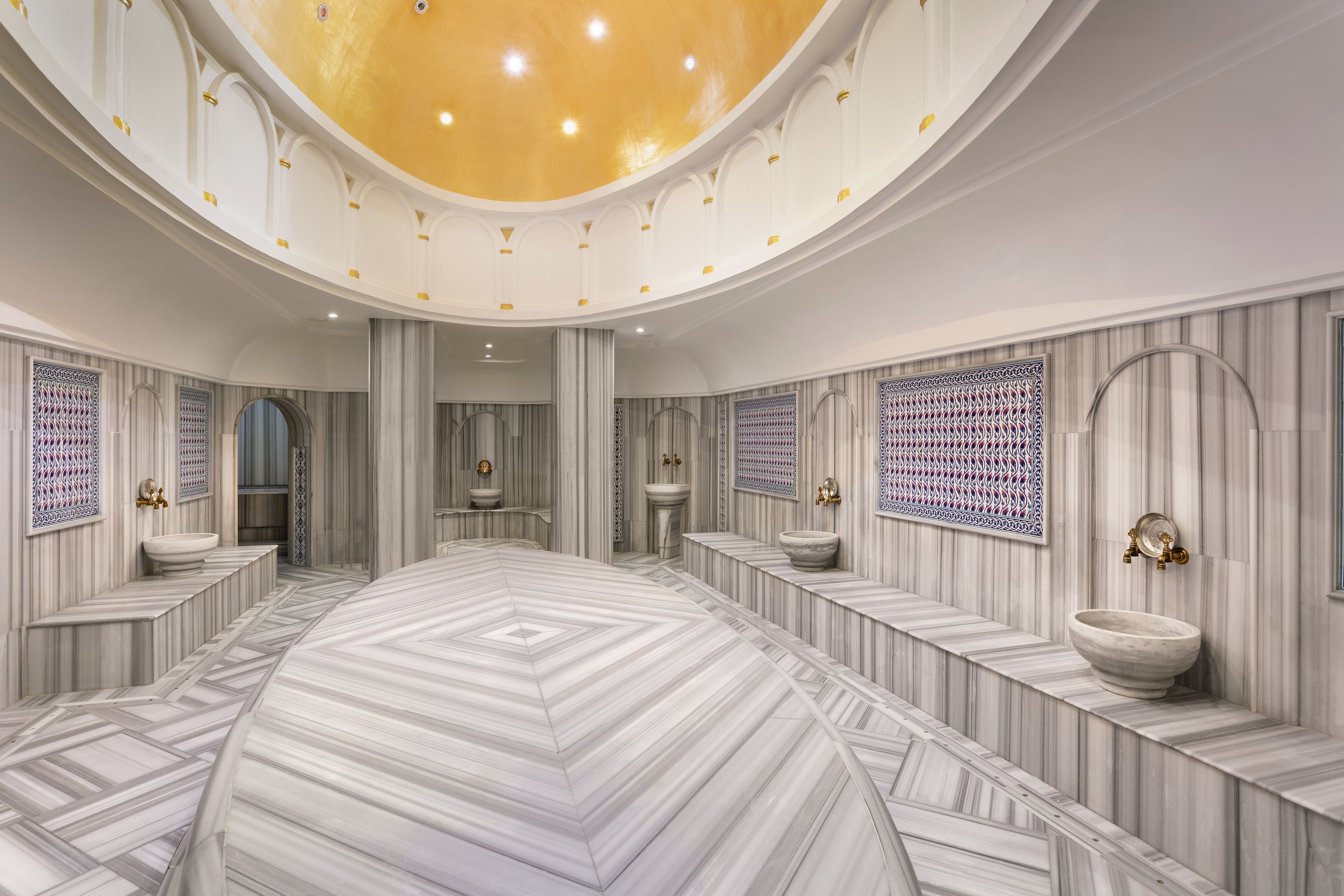 A spacious, elegantly designed bathroom with a large central sink, multiple smaller sinks, and a decorative ceiling.