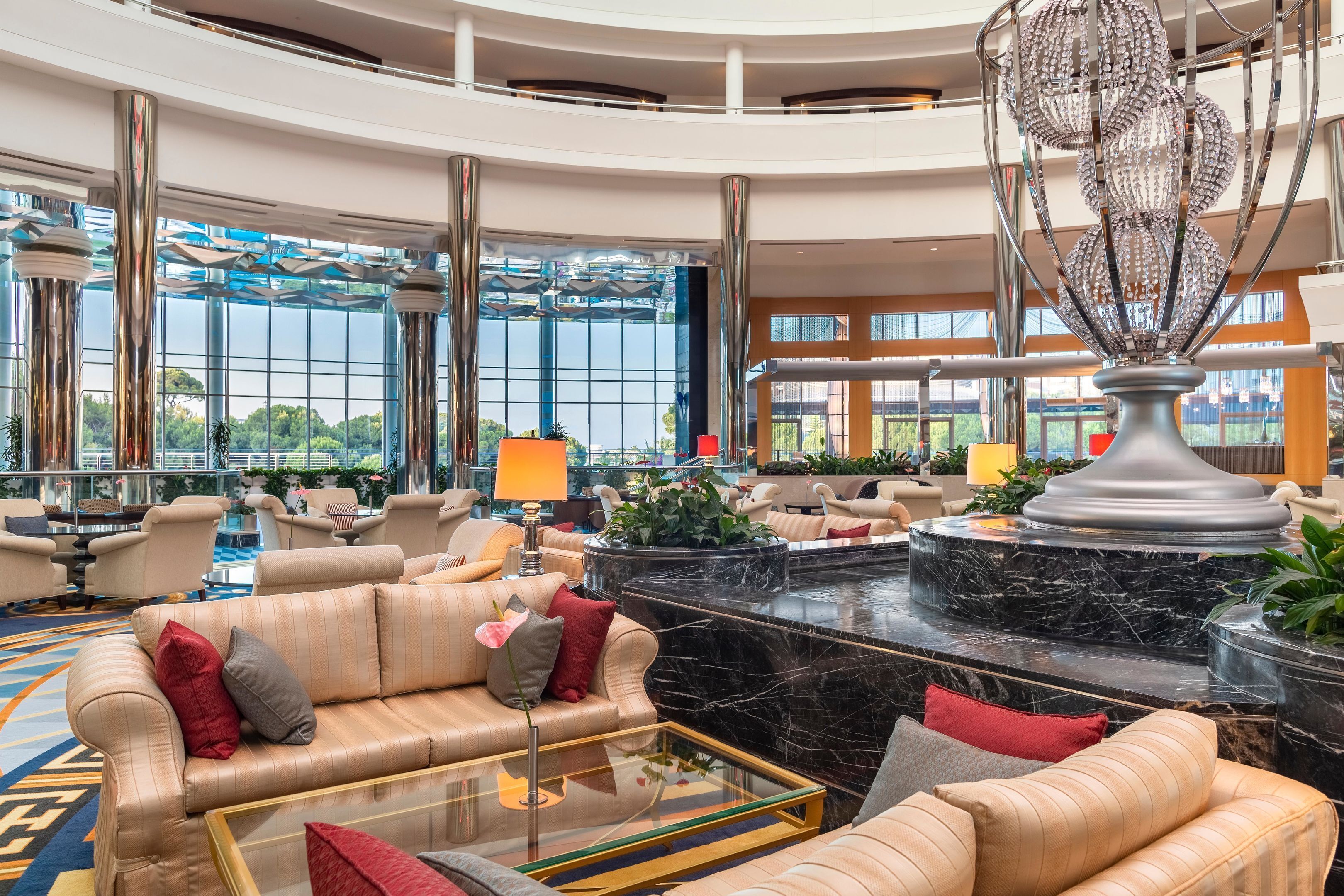 A spacious lobby with a marble reception desk, plush seating, and large windows offering views of greenery.