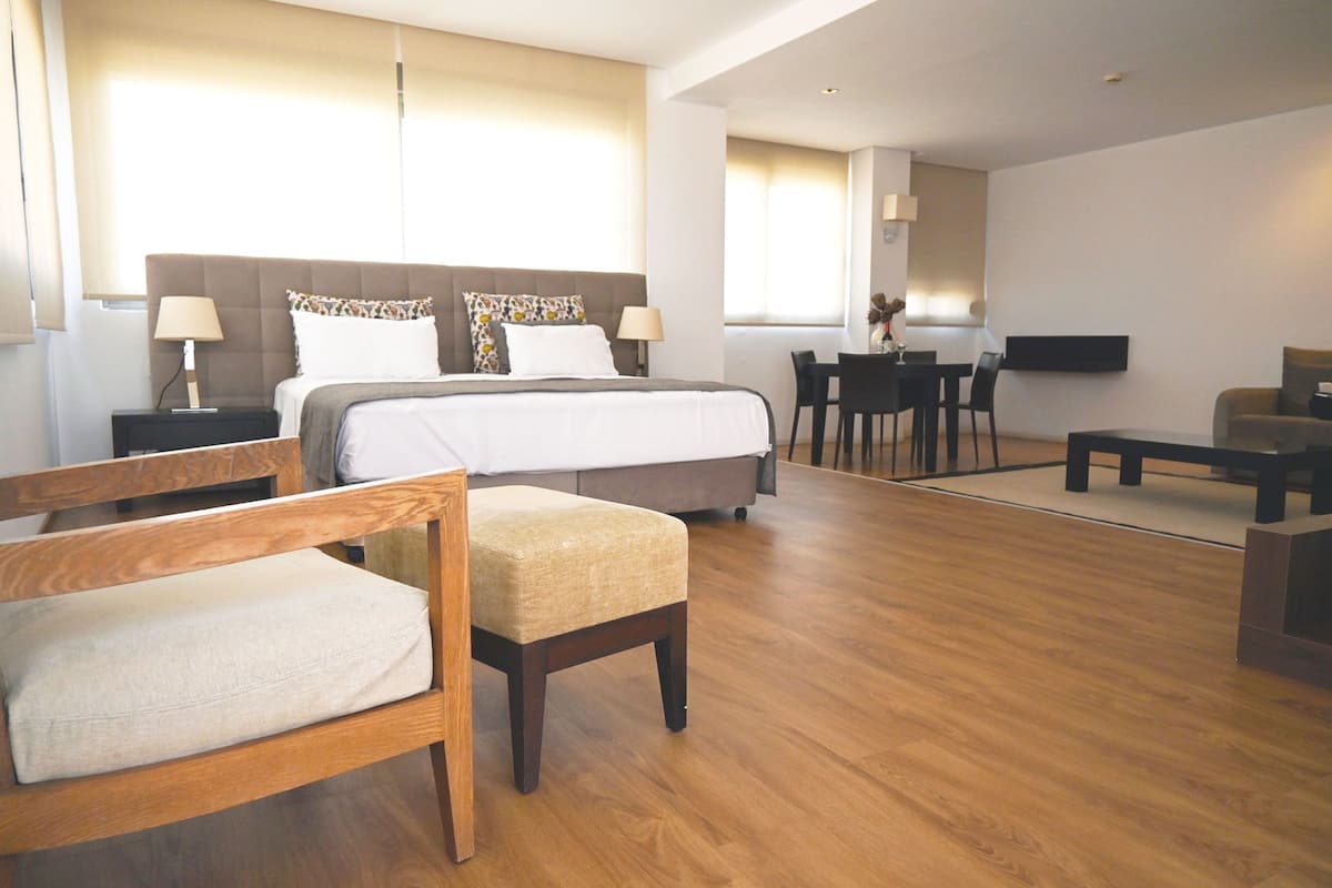Una habitación de hotel moderna con una cama grande, muebles de madera, un rincón de comedor y un televisor.