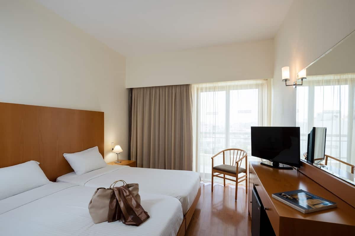 Una habitación de hotel con dos camas, un escritorio con televisor, una silla y una ventana con cortinas.