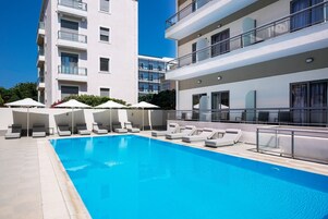 Una piscina al aire libre, sombrillas, sillones reclinables de piscina