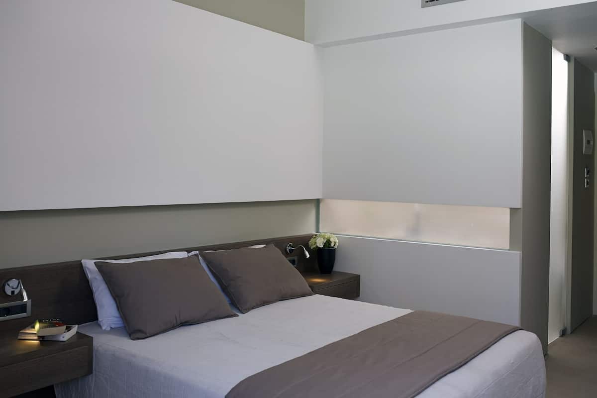 Una habitación de hotel moderna con una cama grande, una mesita de noche con lámpara y una ventana con vistas.