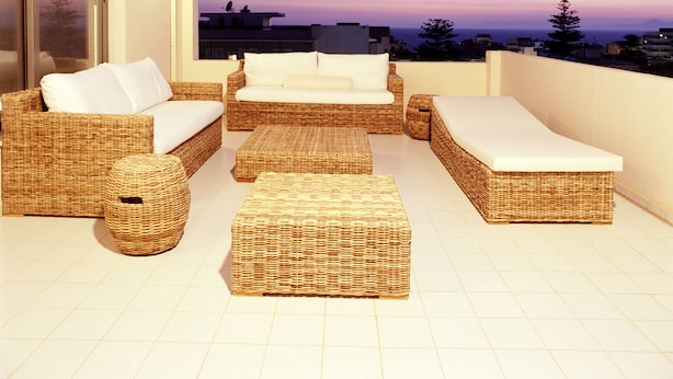 A balcony with wicker furniture, a large window, and a view of the sky and distant buildings. -  Angela Downtown Hotel  (Rhodes)