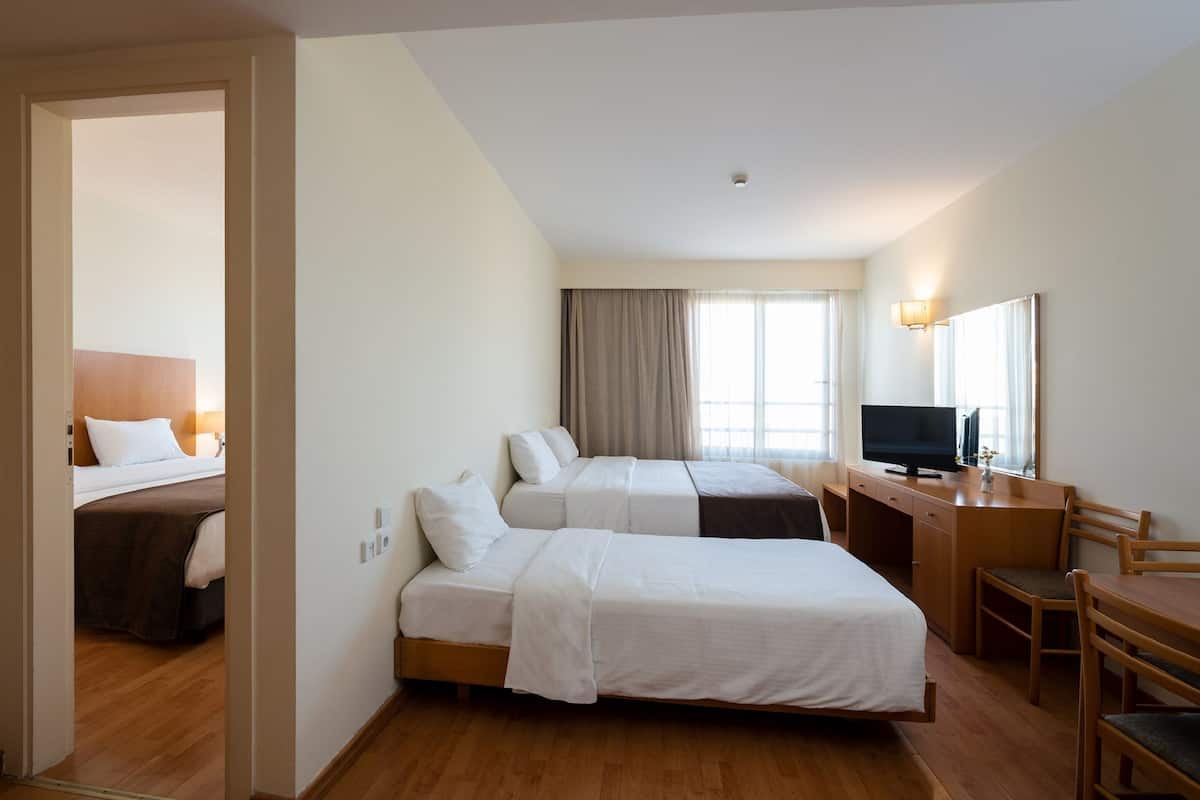 Habitación de hotel con dos camas, un escritorio, un televisor y una ventana con cortinas.