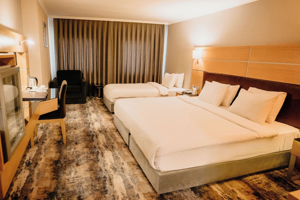 A hotel room with two beds, a desk with a chair, a television, and a large window with curtains.