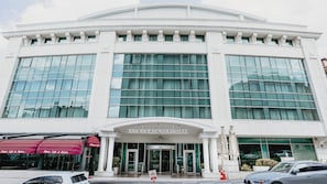 A modern hotel with a curved facade, large glass windows, and a central entrance with a sign reading 'NIKARA PLAZA HOTEL'.