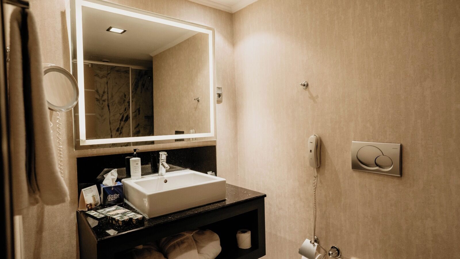 A bathroom with a white sink, a mirror, a towel rack, a toilet, and a wall-mounted phone.