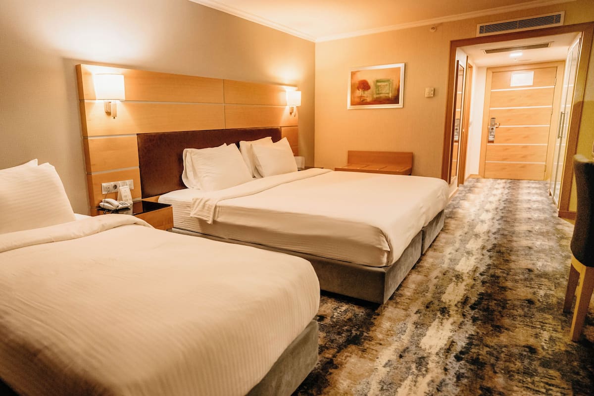 A hotel room with two beds, a nightstand with a phone, a headboard, a wall-mounted light, and a carpeted floor.