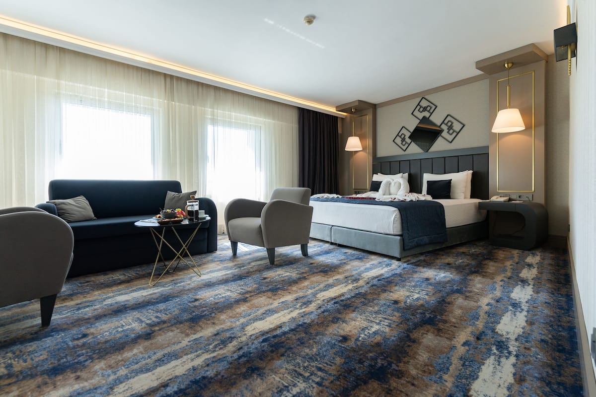 A hotel room with a bed, a sofa, a chair, a small table, and a nightstand.