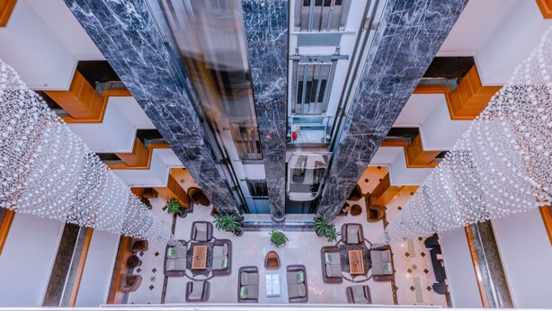 Un hall espacioso con techos altos, columnas de mármol, una zona de estar central con sofás y mesas, y detalles blancos decorativos.