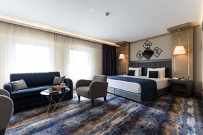 A hotel room with a bed, a sofa, a chair, a small table with a fruit bowl, and a lamp. - Ankara Plaza Hotel (Ankara)
