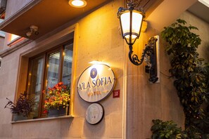 De buitenkant van A'La Sofia Hotel, met een bord met de naam van het hotel, een plaquette die aangeeft dat het een duurzame toeristische accommodatie is, en een bord met het nummer '10'.