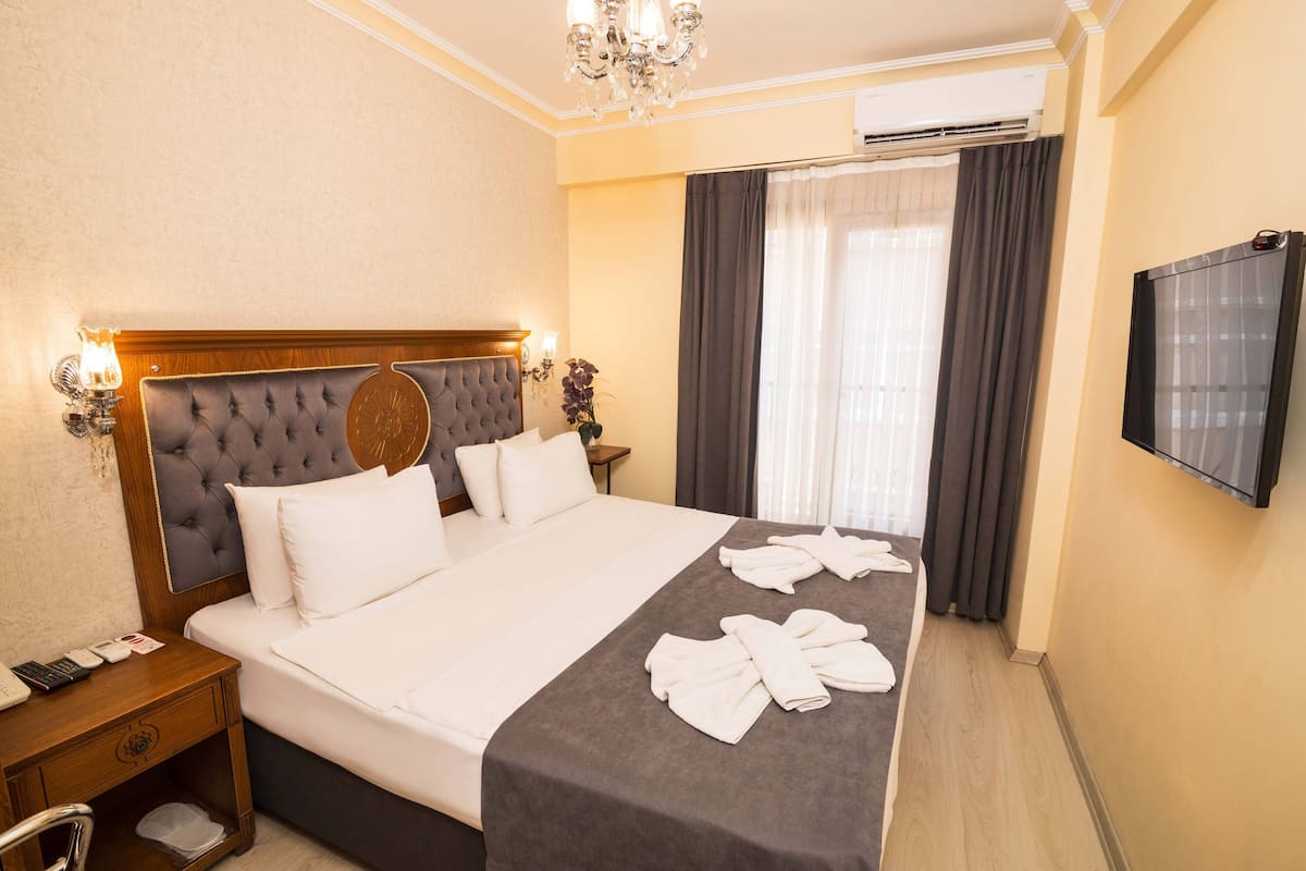 Una habitación de hotel con una cama grande, un cabecero de madera, un televisor de pantalla plana y un escritorio con teléfono.
