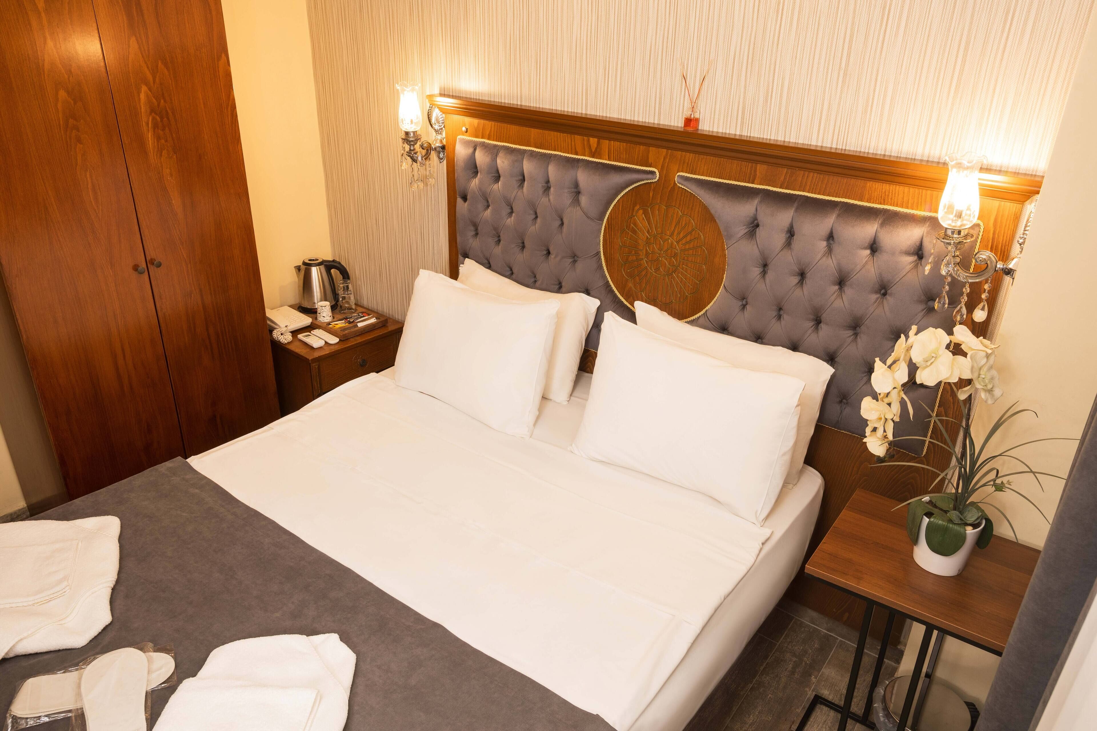A neatly made bed with white linens, a wooden headboard, a bedside table with a lamp, and a small potted plant.